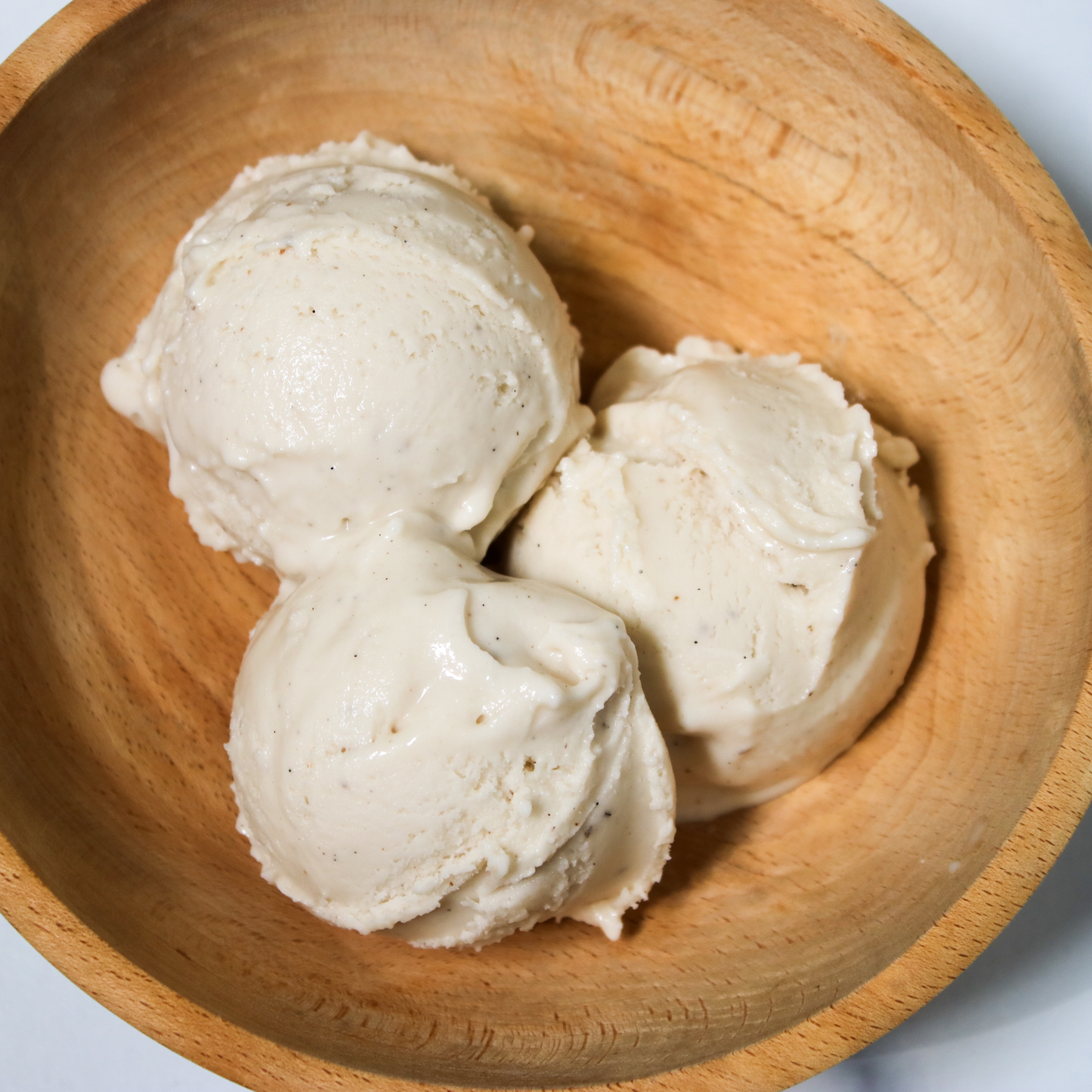 Three scoops of Rose City Creamery Tahitian Vanilla ice cream in a light brown wooden bowl.
