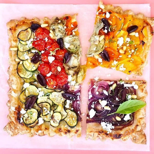 A square vegetable and feta tart with zucchini, artichokes, tomatoes, and bell peppers, cut into quarters.