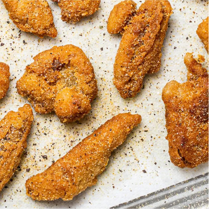 Crispy golden-brown Daring Plant-Based Breaded Chicken Strips coated with seasoning, arranged on a parchment-lined baking sheet.