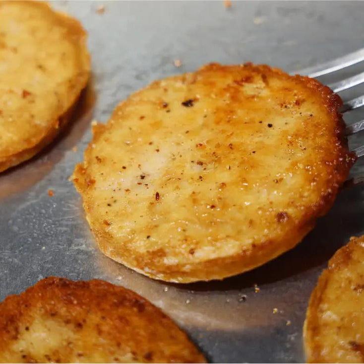 Crispy golden-brown fried Daring Plant-Based Unbreaded Gluten-Free Chicken Patties cooking on a metal pan, with one slice being lifted by a metal spatula.