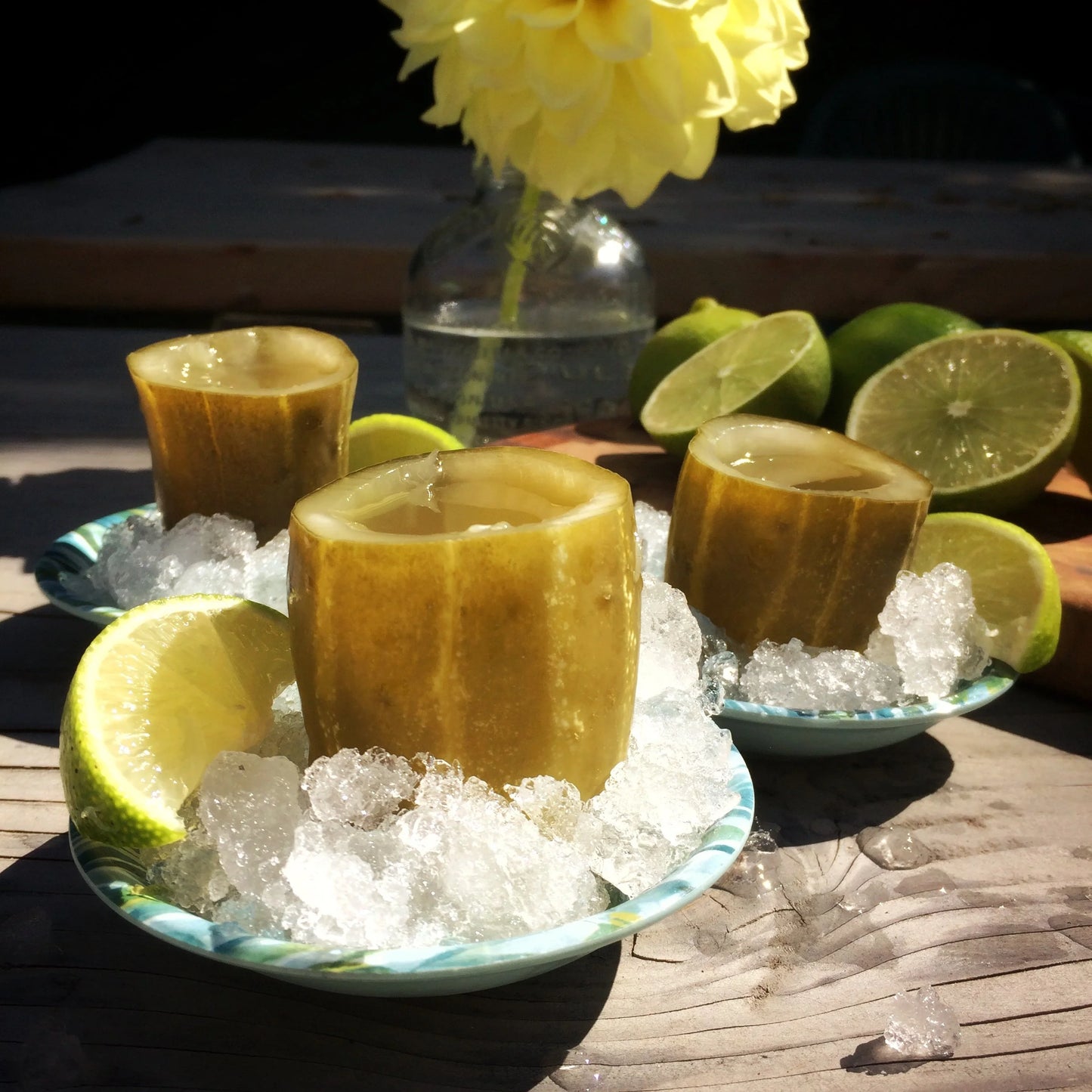 Three hollowed out pickle halves, filled with pickle juice, sitting on ice next to a lime.