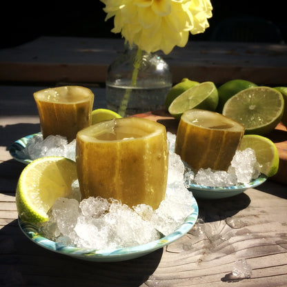 Three hollowed out pickle halves, filled with pickle juice, sitting on ice next to a lime.