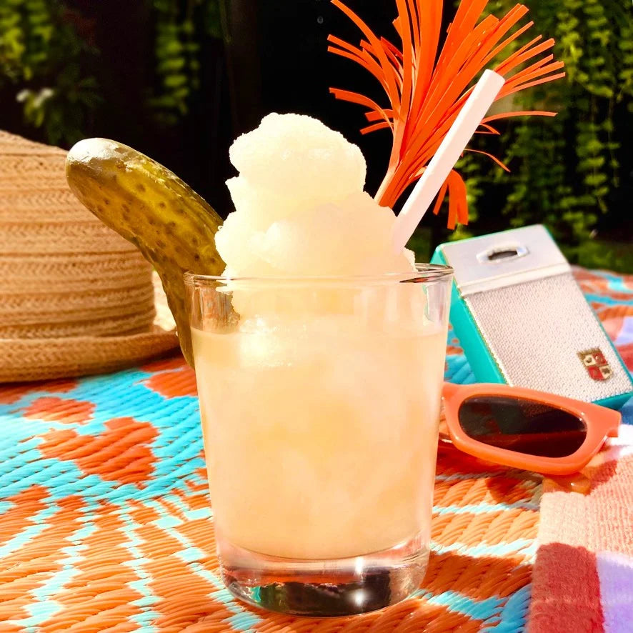 A citrus slushie with a split pickle sitting on the rim.
