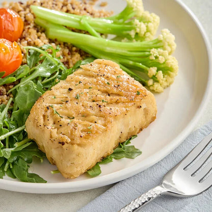 A plated cooked Oshi Plant-Based White Fish Fillet served on a bed of greens with broccoli, cauliflower, and grains, with a fork on a light blue napkin.