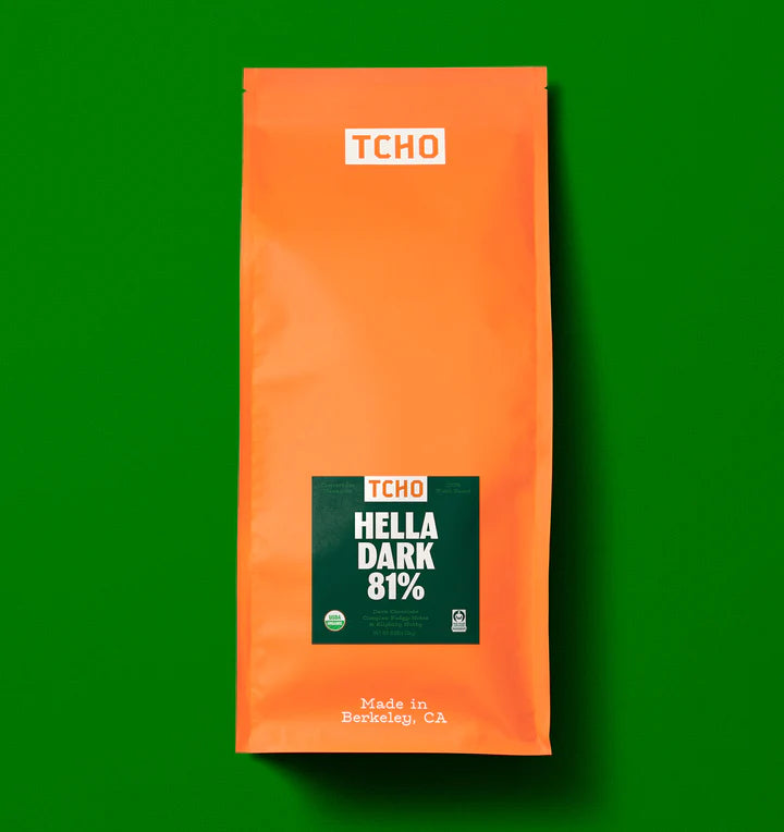 An orange bag of TCHO Hella Dark 81% chocolate centered on a solid green background.