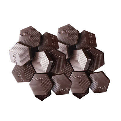 A pile of hexagonal-shaped TCHO Mighty Mosaic chocolate couvertures with the brand name 'TCHO' inscribed on them.
