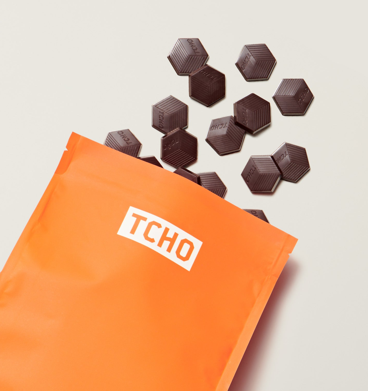 Orange TCHO chocolate packaging with TCHO Mighty Mosaic hexagonal chocolates on a light background