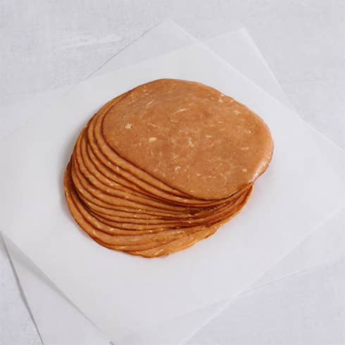 Stack of thinly sliced Tofurky Smoked Ham on white parchment paper