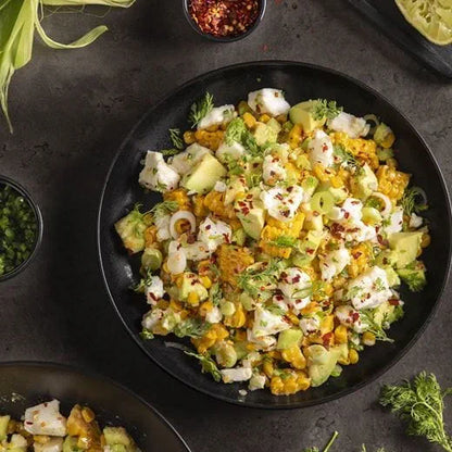 A plate filled with roasted corn, avocado, green onions, herbs, and Violife Just Like Feta crumbles